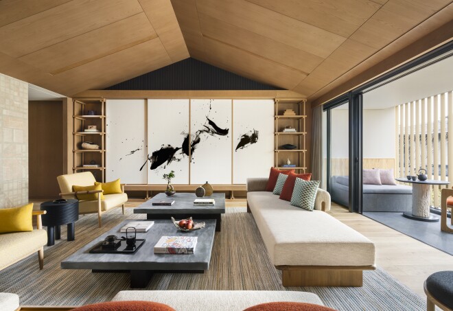 The living room of the Three Bedroom Penthouse Suite at the Six Senses Kyoto features a large black and white brush painting,  large white sofas, and a large terrace.