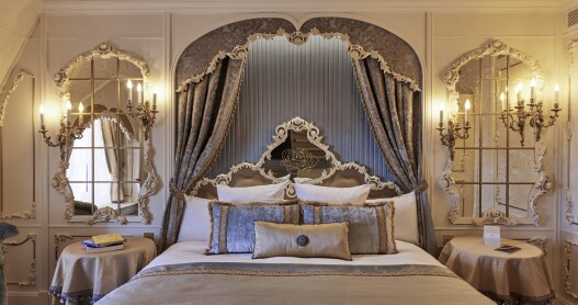 An ornate bed flanked by mirrors and candelabra-style lights in the Beauty and the Beast-themed Princely suite at Disneyland Hotel, Disneyland Paris