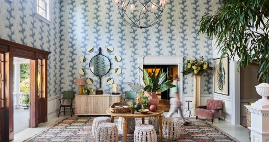 A hotel lobby with boldly patterned wallpaper, potted trees, mirrors and artwork on the walls, and a patterned area rug