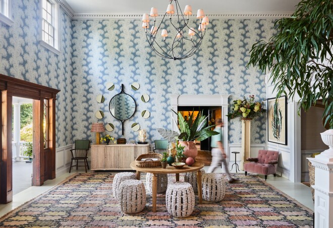 A hotel lobby with boldly patterned wallpaper, potted trees, mirrors and artwork on the walls, and a patterned area rug