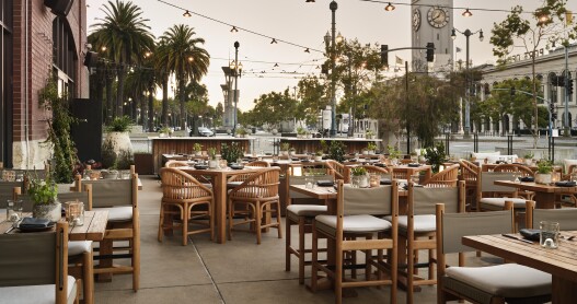 Terrene bar at 1 hotel in San Francisco with palm trees and the ferry building in the background. There are no people on the patio.