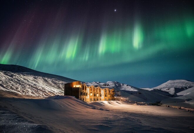 Hotel building with three stories in the middle of a snowy landscape with the northern lights overhead